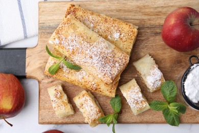 Photo of Tasty apple strudels with powdered sugar, fruits and mint on white table, flat lay