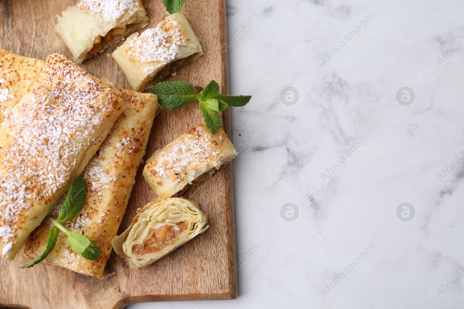 Photo of Tasty apple strudels with powdered sugar and mint on white marble table, top view. Space for text