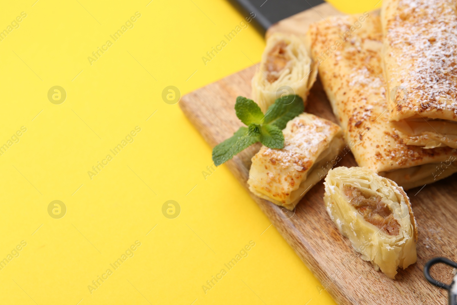 Photo of Tasty apple strudels with powdered sugar and mint on yellow background, closeup. Space for text