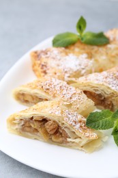 Photo of Tasty apple strudels with powdered sugar and mint on table, closeup