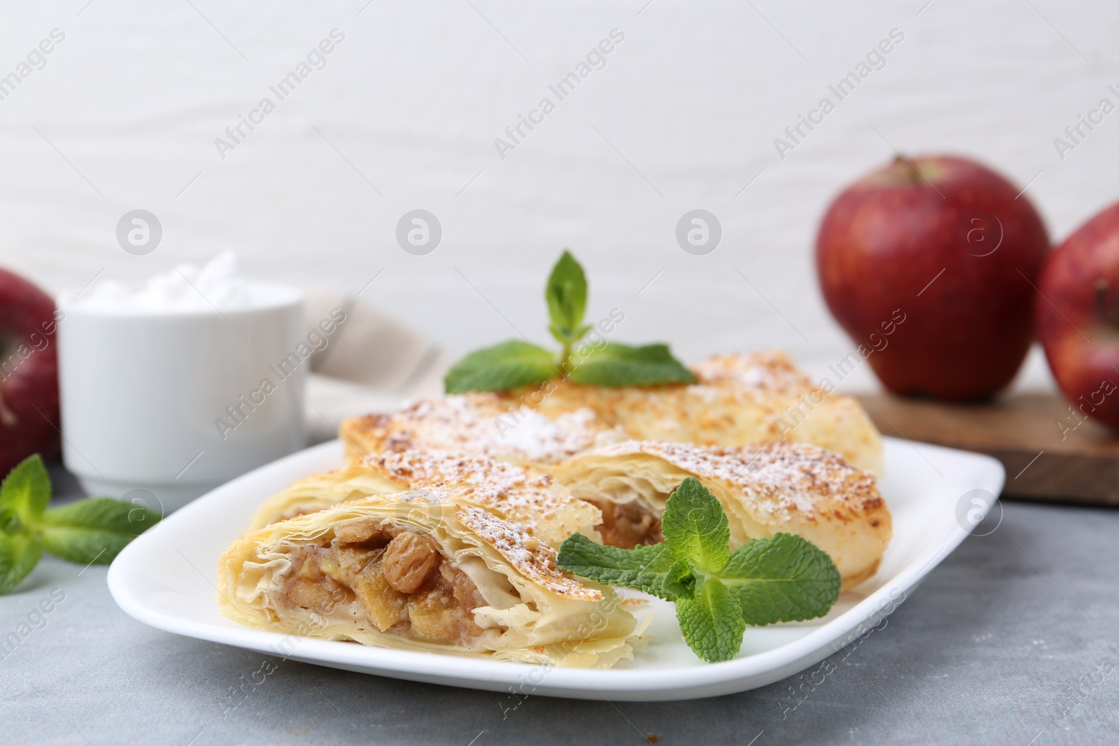 Photo of Tasty apple strudels with powdered sugar and mint on light grey table, closeup