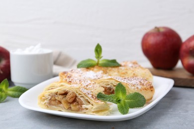 Tasty apple strudels with powdered sugar and mint on light grey table, closeup