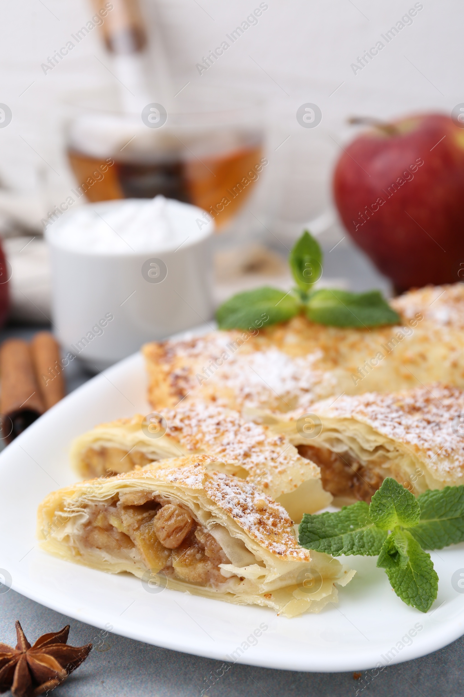 Photo of Tasty apple strudels with powdered sugar, mint and spices on table, closeup