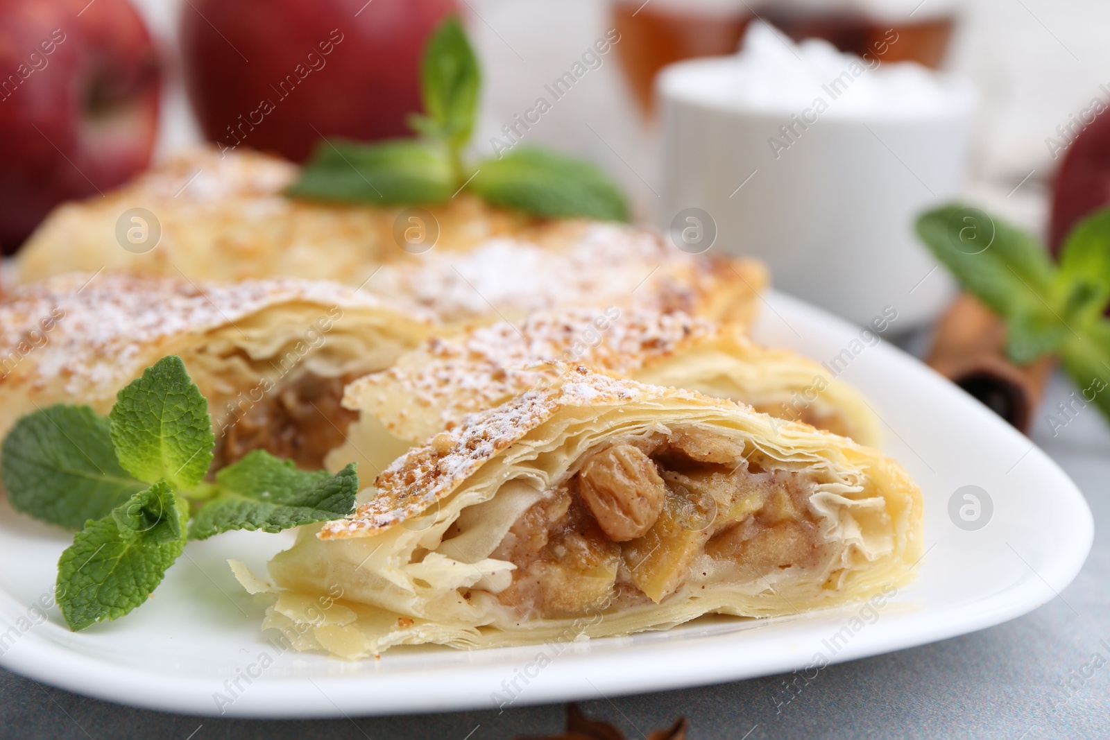 Photo of Tasty apple strudels with powdered sugar and mint on light grey table, closeup