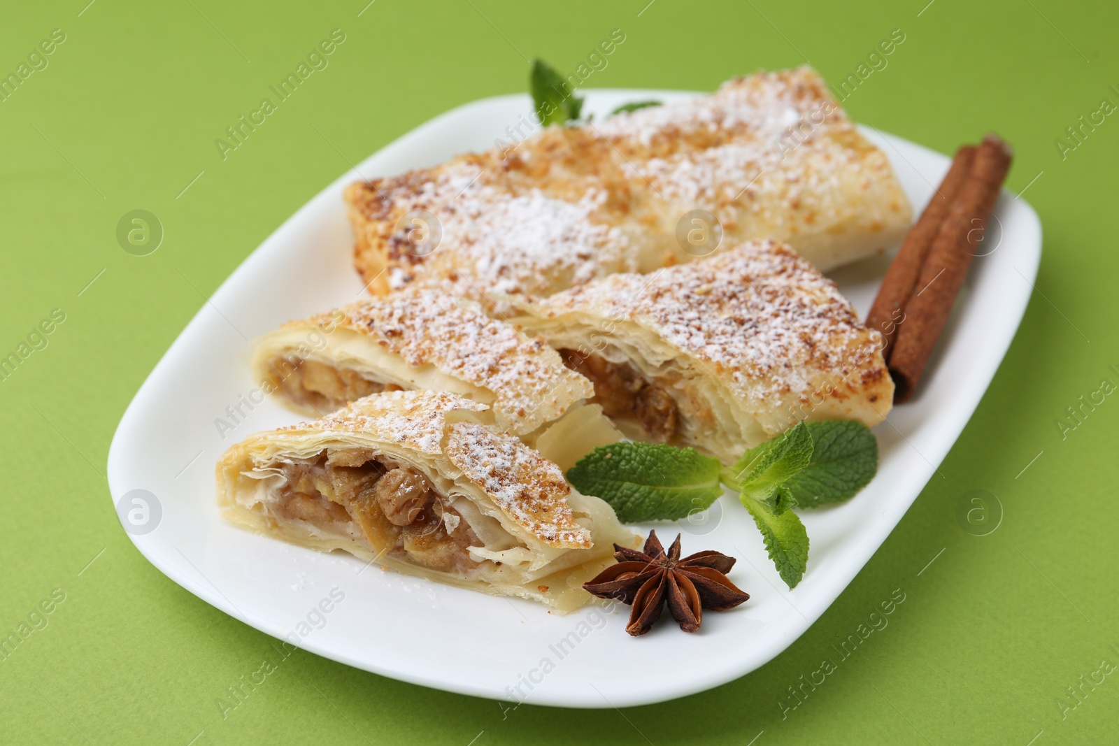 Photo of Tasty apple strudels with powdered sugar, mint and spices on green background, closeup