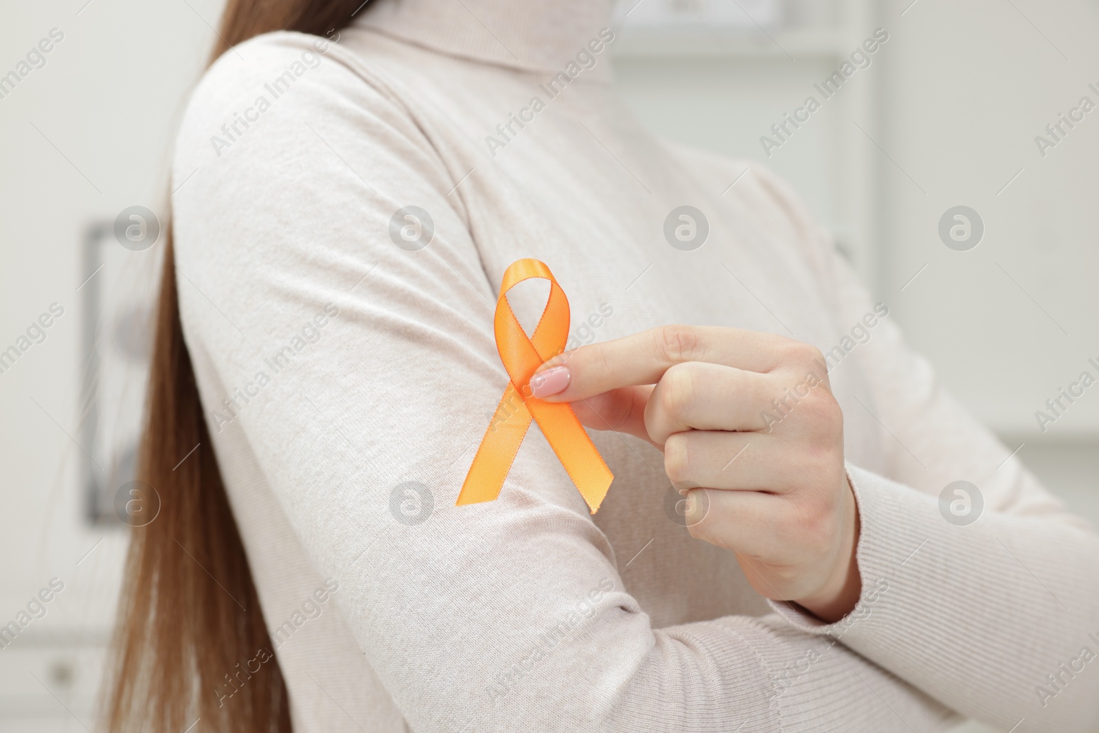 Photo of Multiple Sclerosis awareness. Young woman holding orange ribbon indoors, closeup