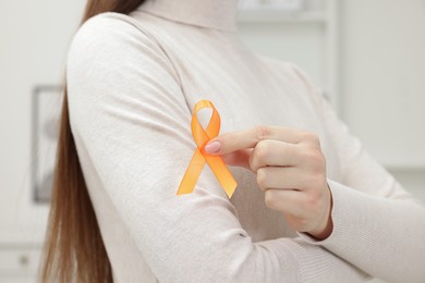 Multiple Sclerosis awareness. Young woman holding orange ribbon indoors, closeup