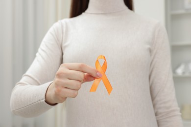 Multiple Sclerosis awareness. Young woman holding orange ribbon indoors, closeup