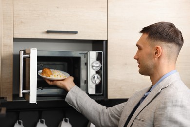 Man putting plate with lunch into microwave in kitchen