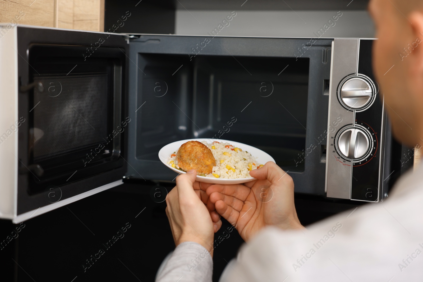 Photo of Man putting plate with lunch into microwave in kitchen, closeup