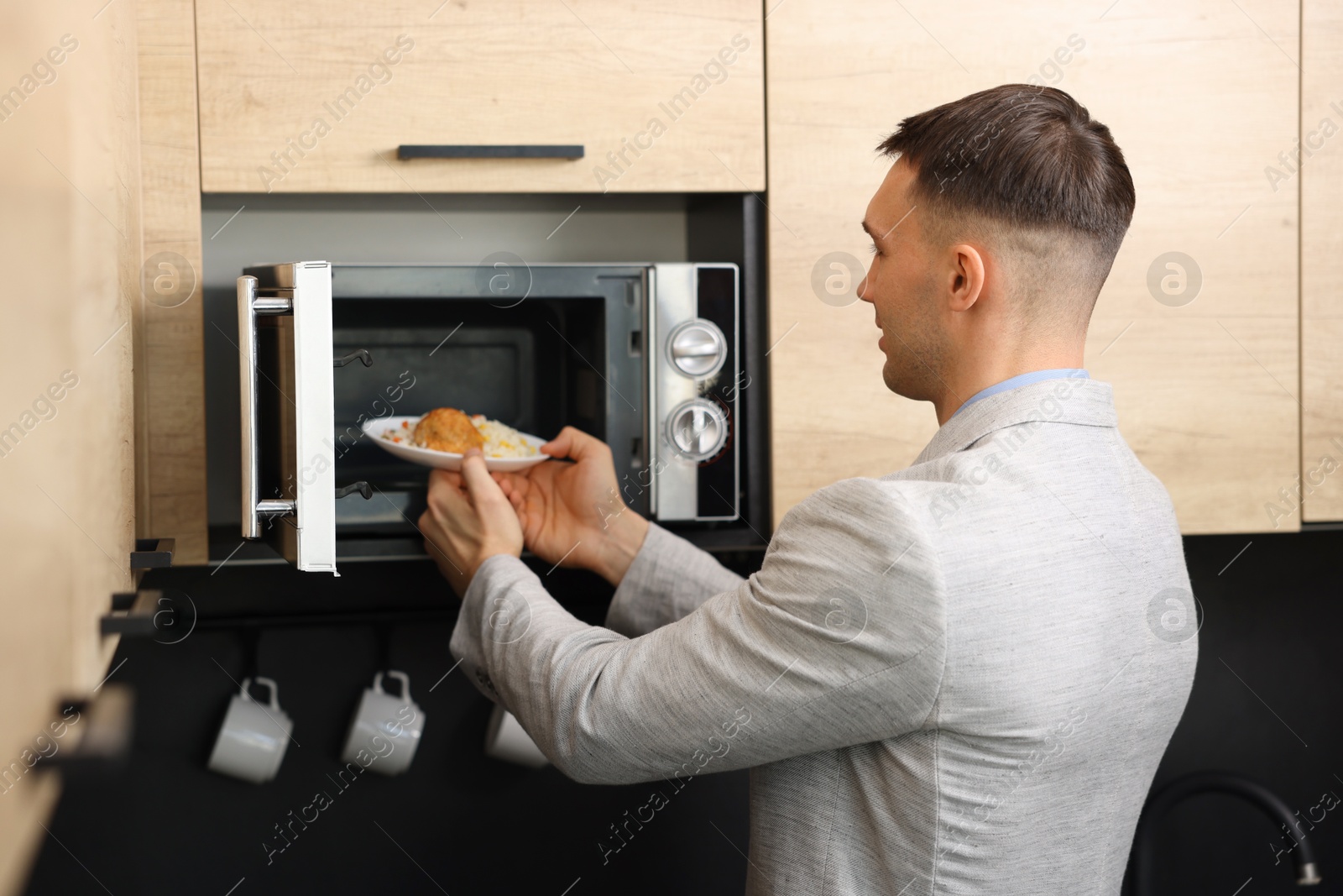 Photo of Man putting plate with lunch into microwave in kitchen