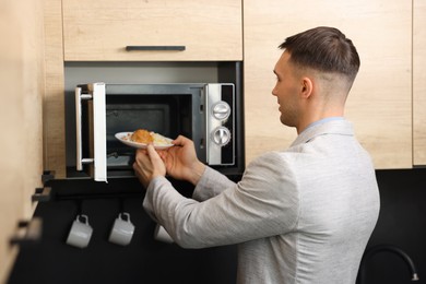 Man putting plate with lunch into microwave in kitchen