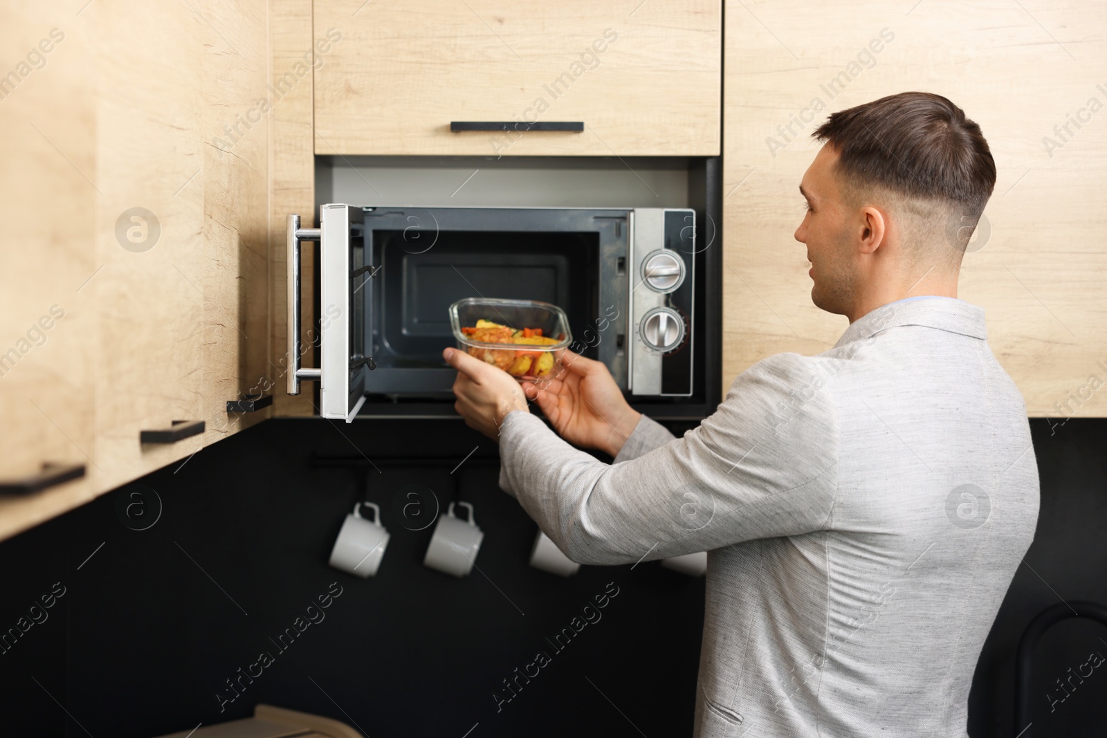 Photo of Man putting container with lunch into microwave in kitchen