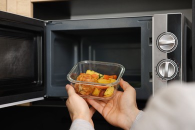 Man putting container with lunch into microwave in kitchen, closeup