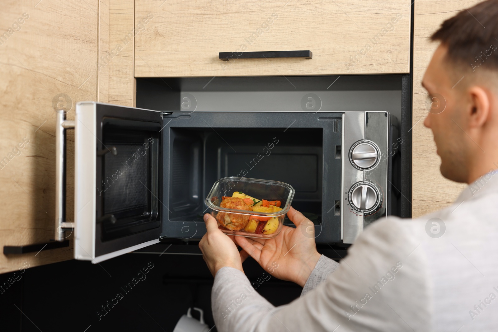 Photo of Man putting container with lunch into microwave in kitchen, closeup