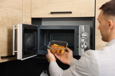 Photo of Man putting container with lunch into microwave in kitchen, closeup