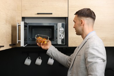 Photo of Man putting container with lunch into microwave in kitchen