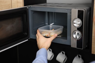 Photo of Man putting container with lunch into microwave in kitchen, closeup