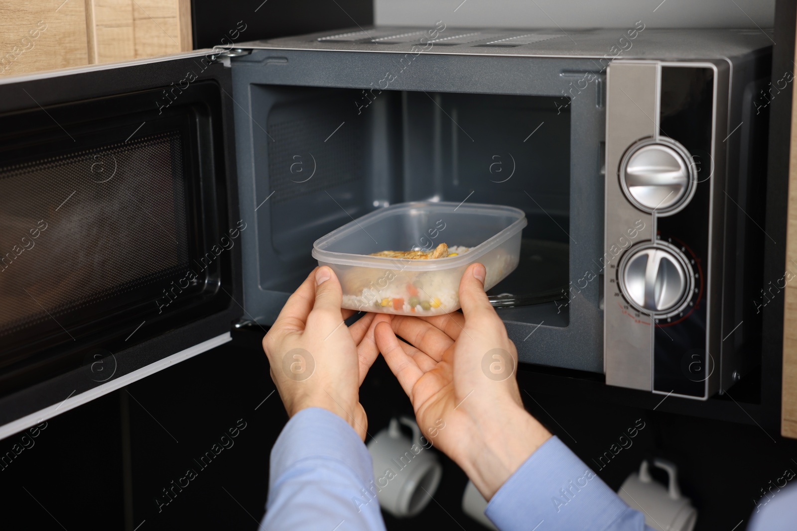 Photo of Man putting container with lunch into microwave in kitchen, closeup