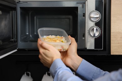 Photo of Man putting container with lunch into microwave in kitchen, closeup