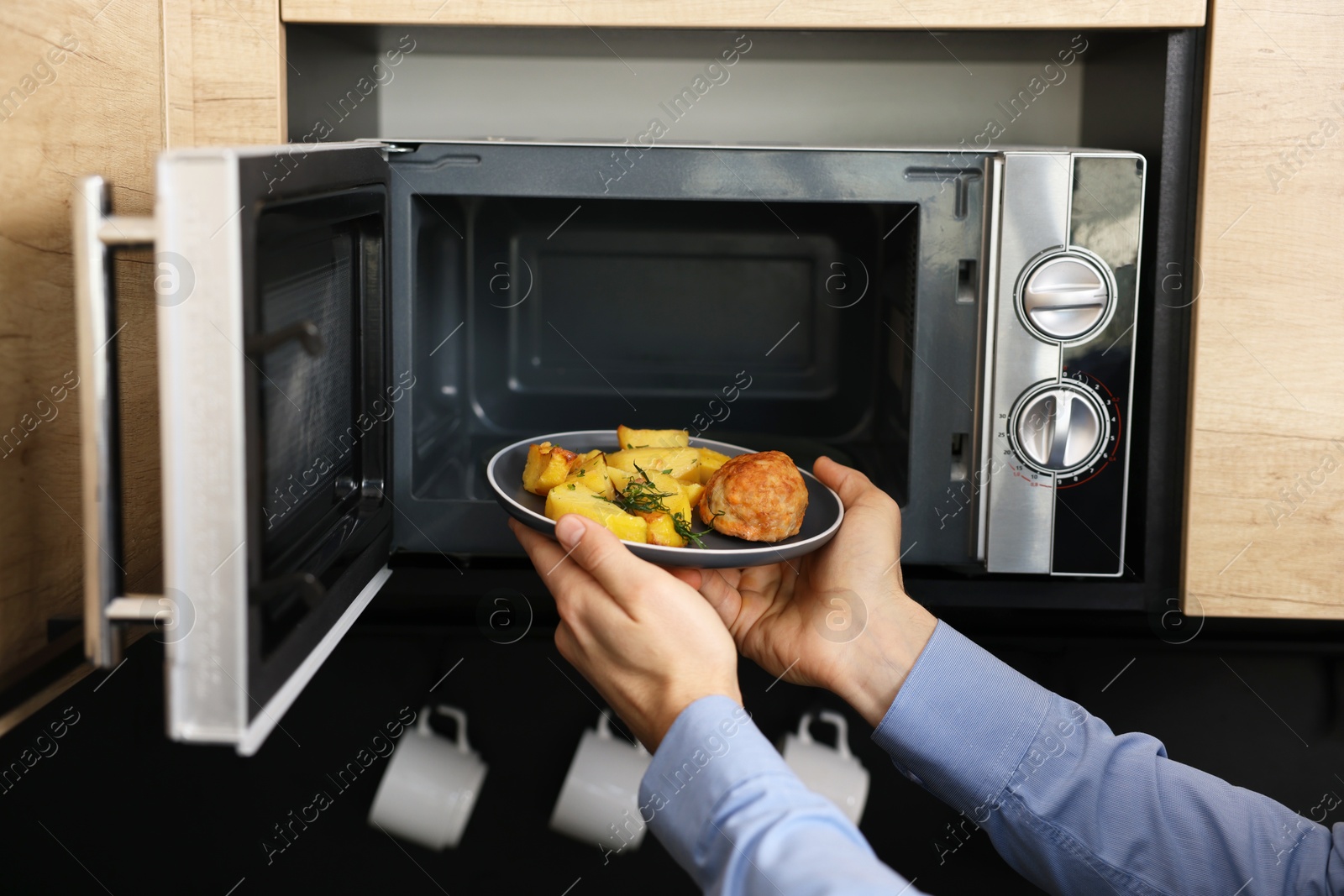 Photo of Man putting plate with lunch into microwave in kitchen, closeup