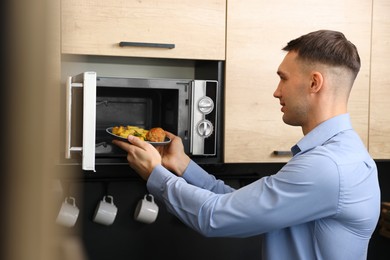 Man putting plate with lunch into microwave in kitchen