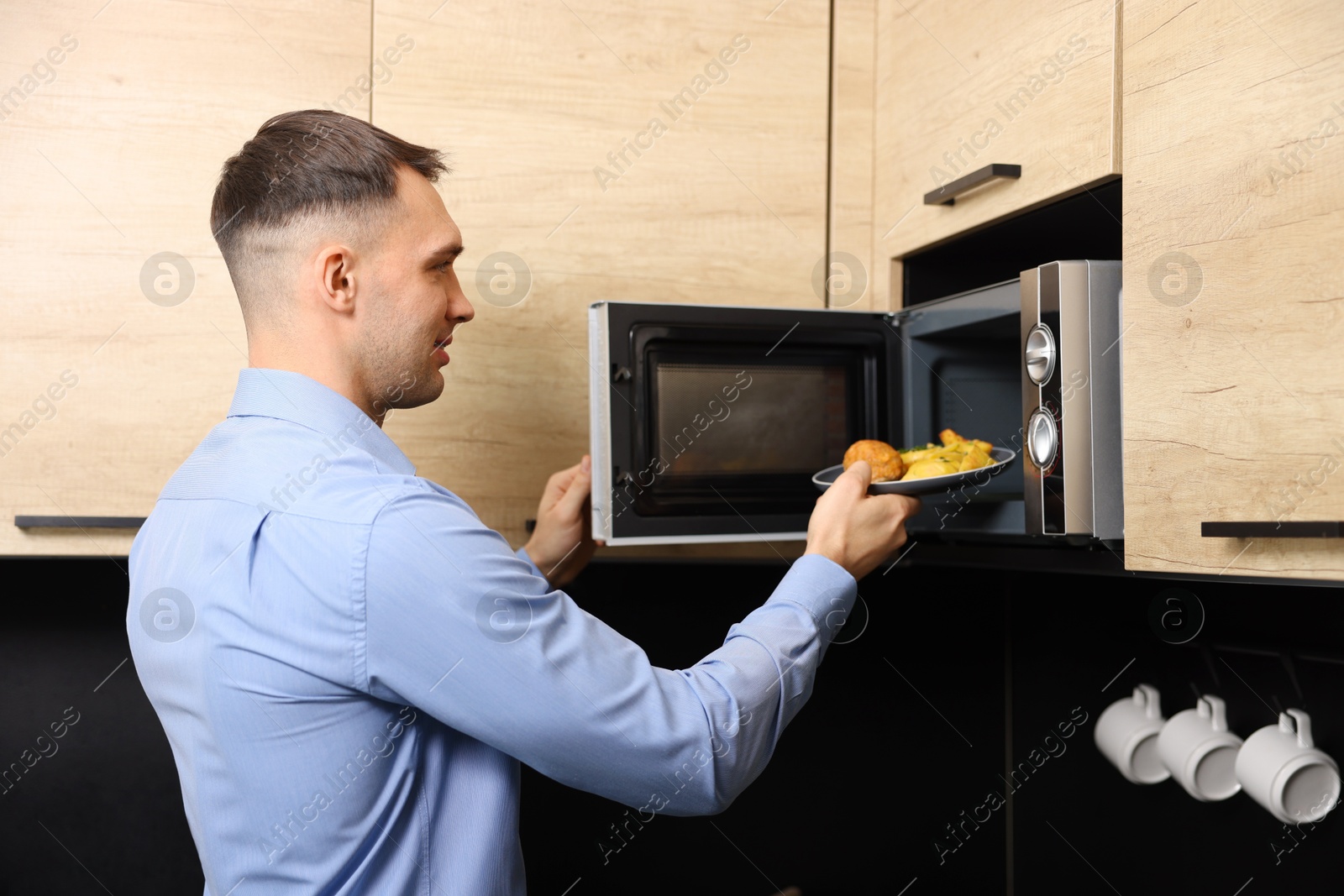 Photo of Man putting plate with lunch into microwave in kitchen