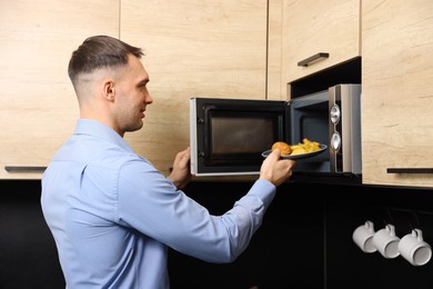 Photo of Man putting plate with lunch into microwave in kitchen