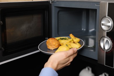 Man putting plate with lunch into microwave in kitchen, closeup