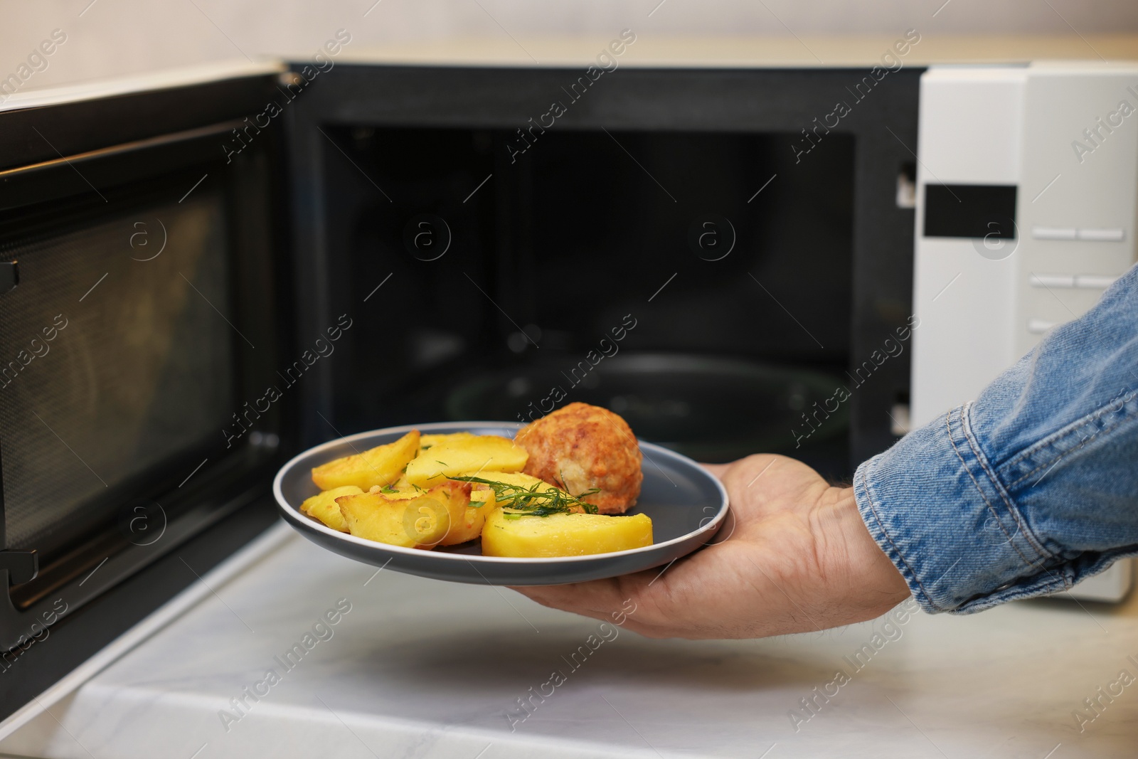 Photo of Man putting plate with lunch into microwave in kitchen, closeup