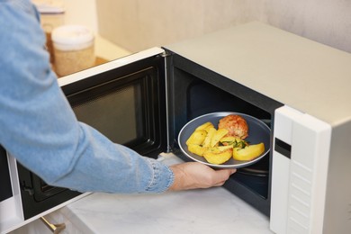 Man putting plate with lunch into microwave in kitchen, closeup