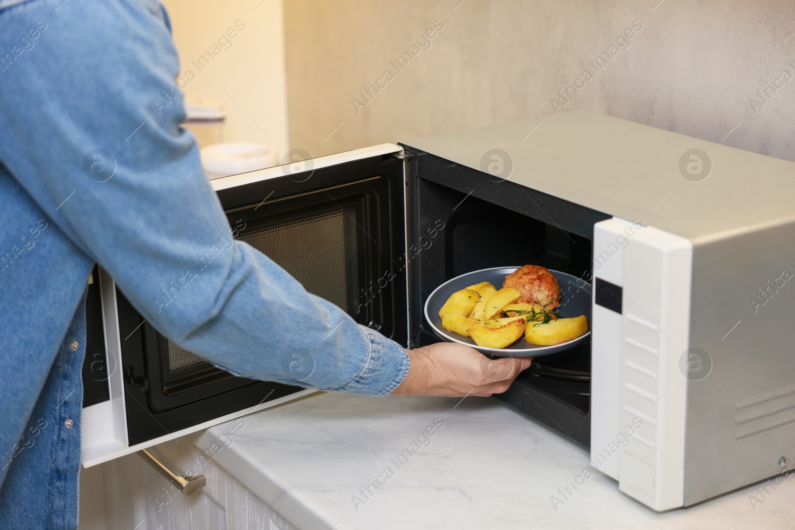 Photo of Man putting plate with lunch into microwave in kitchen, closeup