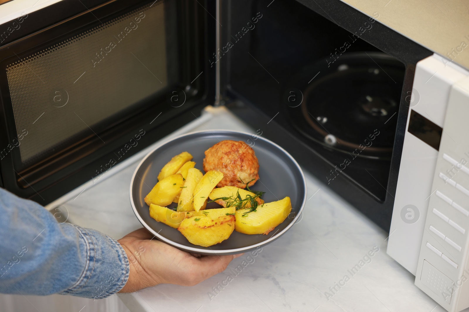 Photo of Man putting plate with lunch into microwave in kitchen, closeup