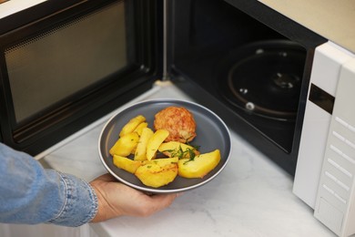 Man putting plate with lunch into microwave in kitchen, closeup