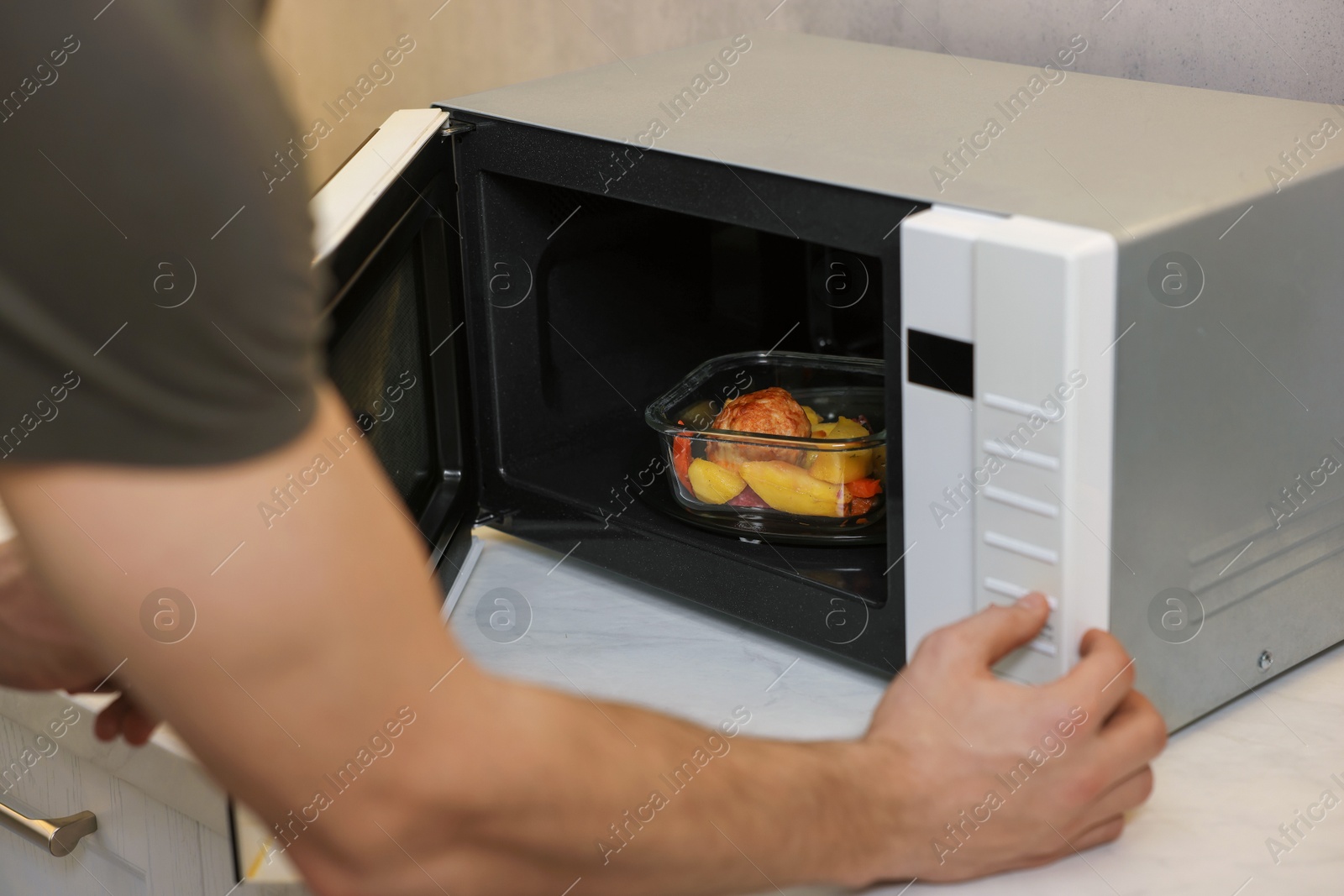 Photo of Man putting container with lunch into microwave in kitchen, closeup