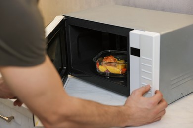 Photo of Man putting container with lunch into microwave in kitchen, closeup