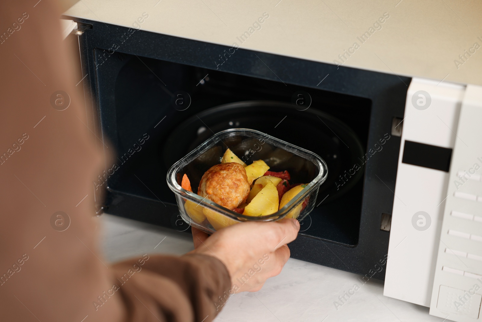 Photo of Man putting container with lunch into microwave in kitchen, closeup