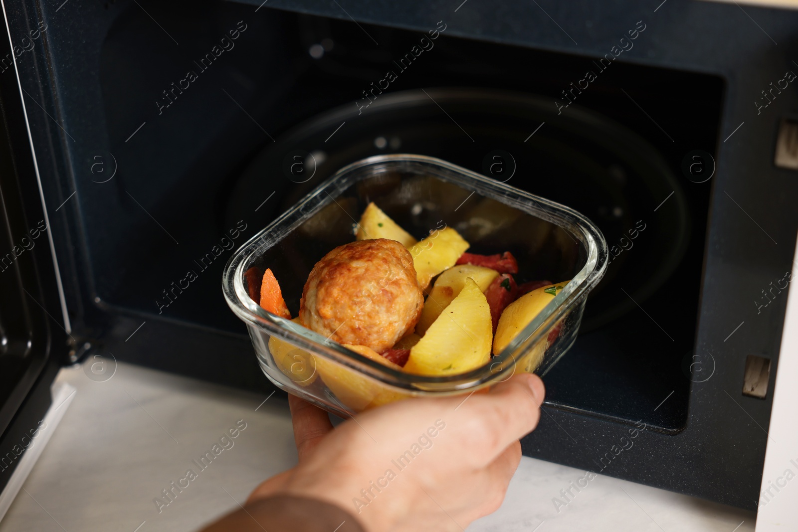 Photo of Man putting container with lunch into microwave in kitchen, closeup