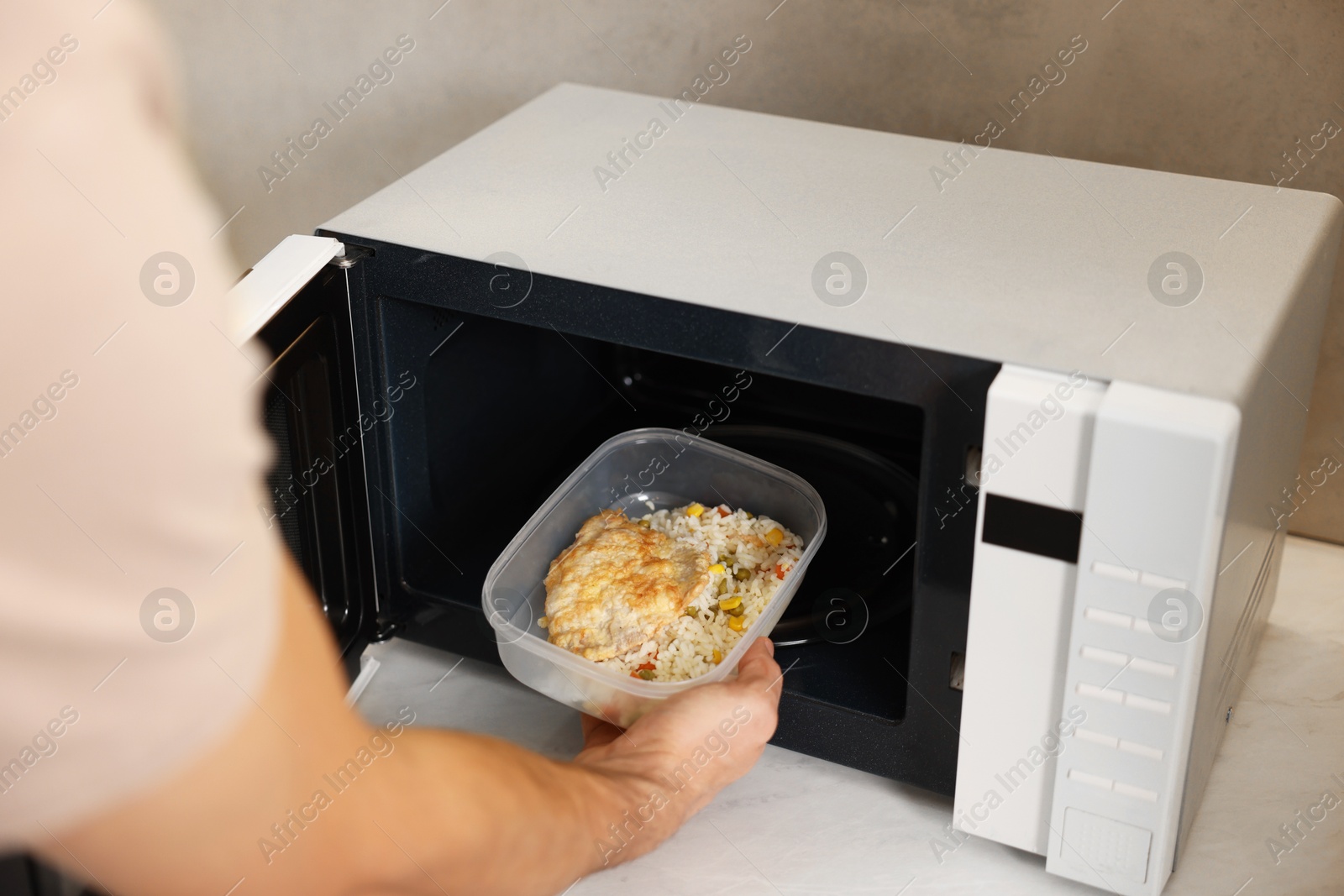 Photo of Man putting container with lunch into microwave in kitchen, closeup