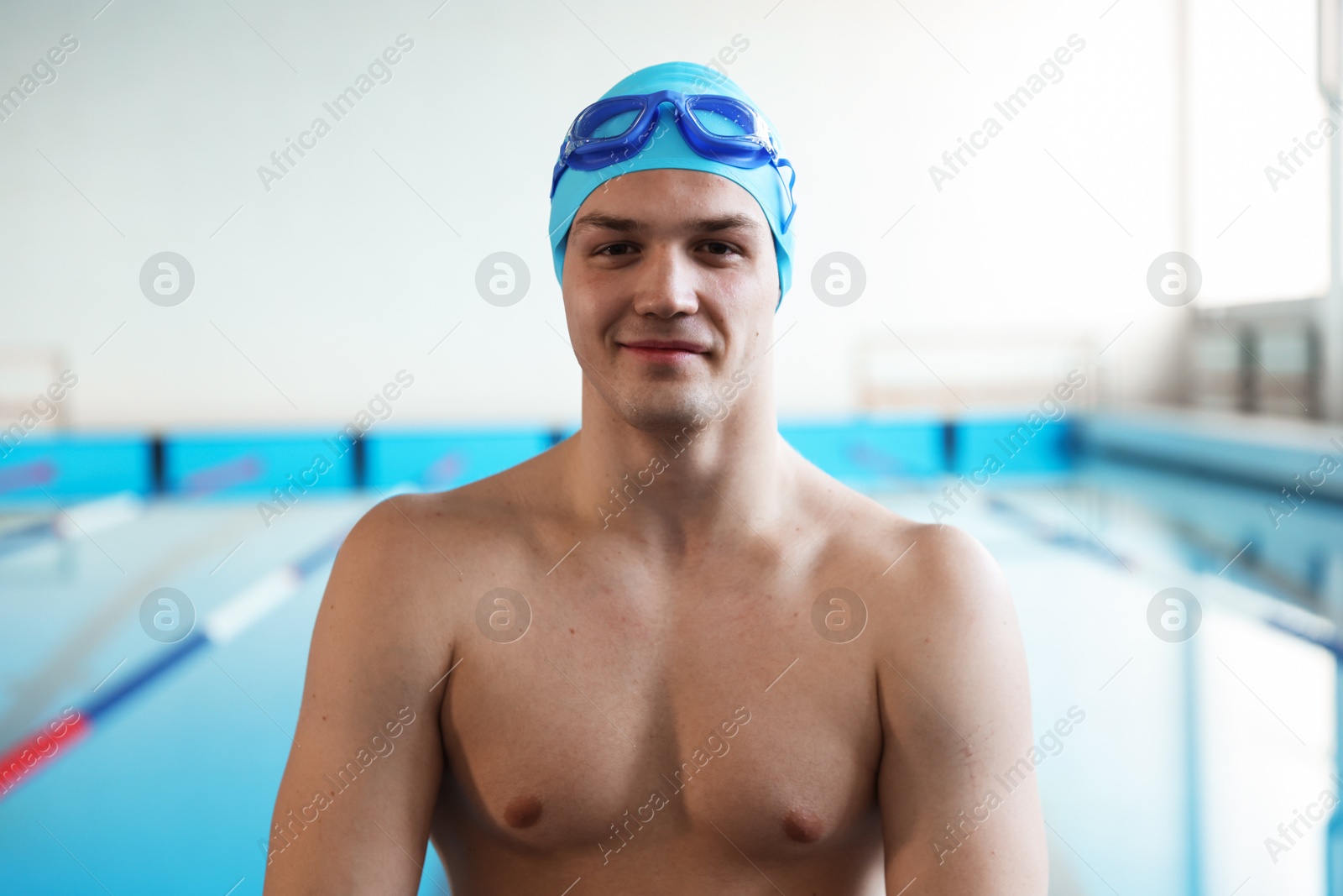 Photo of Young man with cap and goggles near swimming pool indoors