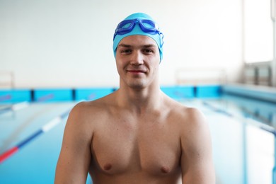 Young man with cap and goggles near swimming pool indoors