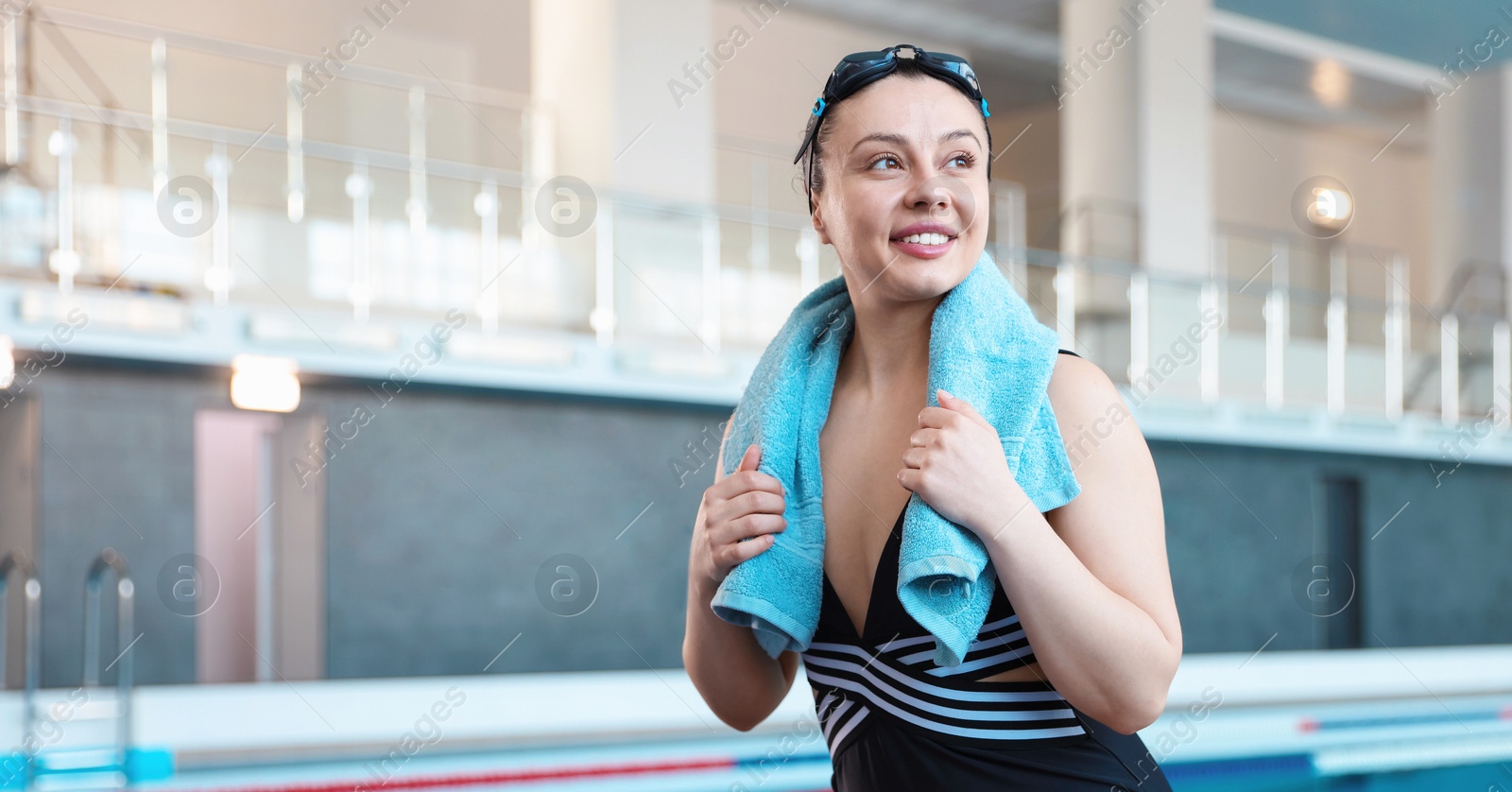 Photo of Happy woman with goggles, swimsuit and towel near swimming pool indoors