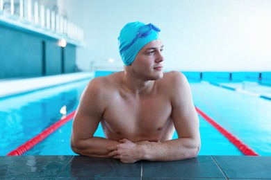 Young man with cap and goggles in swimming pool indoors