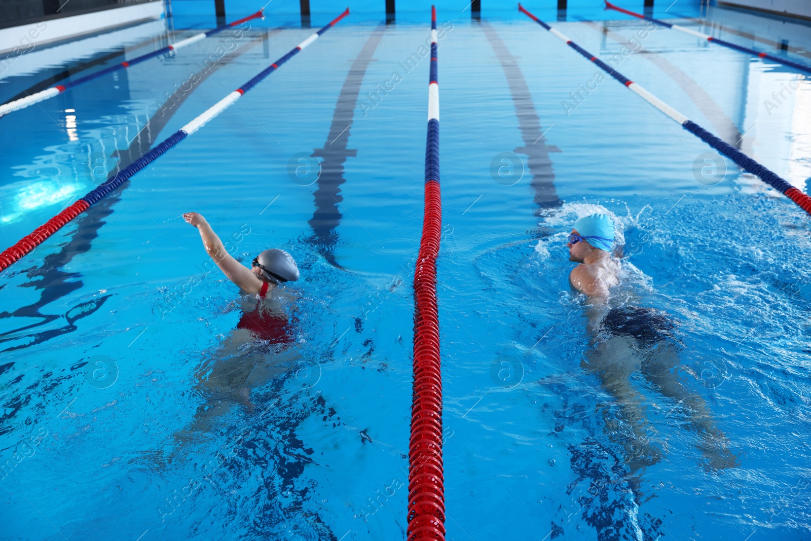 Photo of Young man and woman swimming in pool indoors