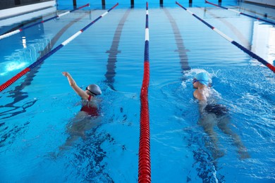 Young man and woman swimming in pool indoors