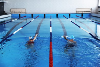 Photo of Young man and woman swimming in pool indoors