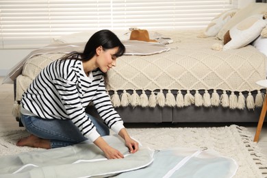 Photo of Woman putting clothes into garment cover on floor indoors