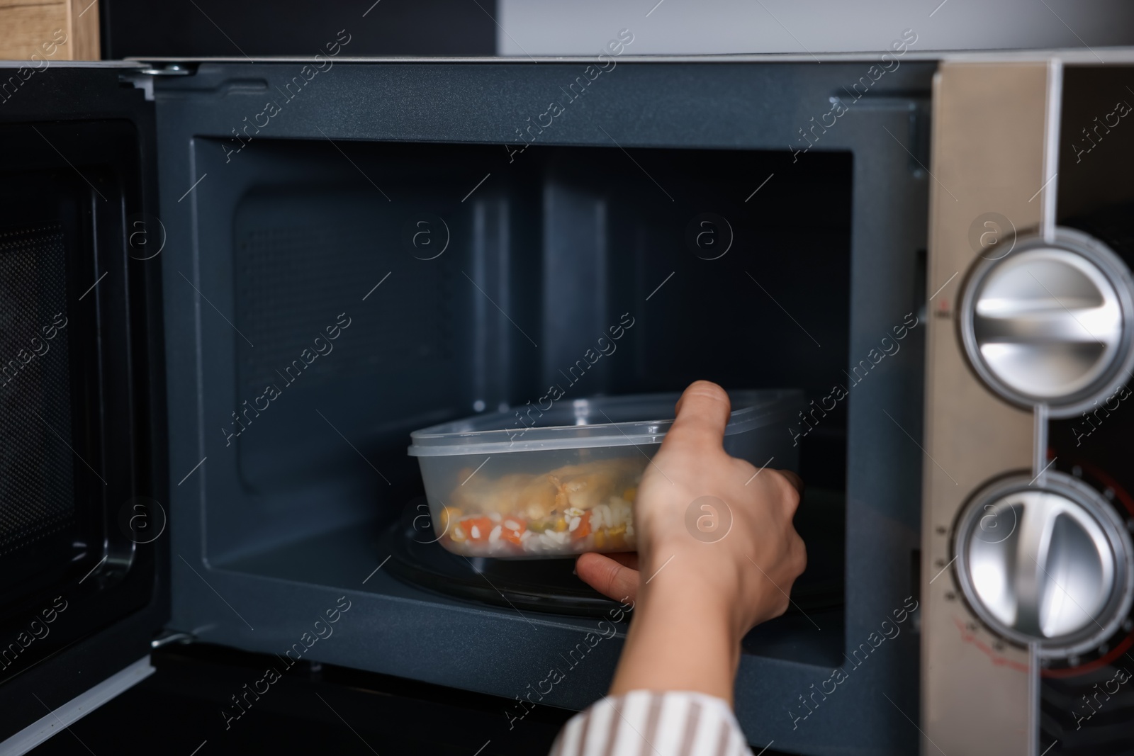 Photo of Woman putting container with lunch into microwave indoors, closeup