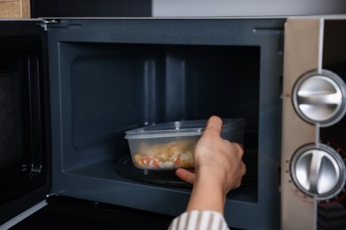 Woman putting container with lunch into microwave indoors, closeup