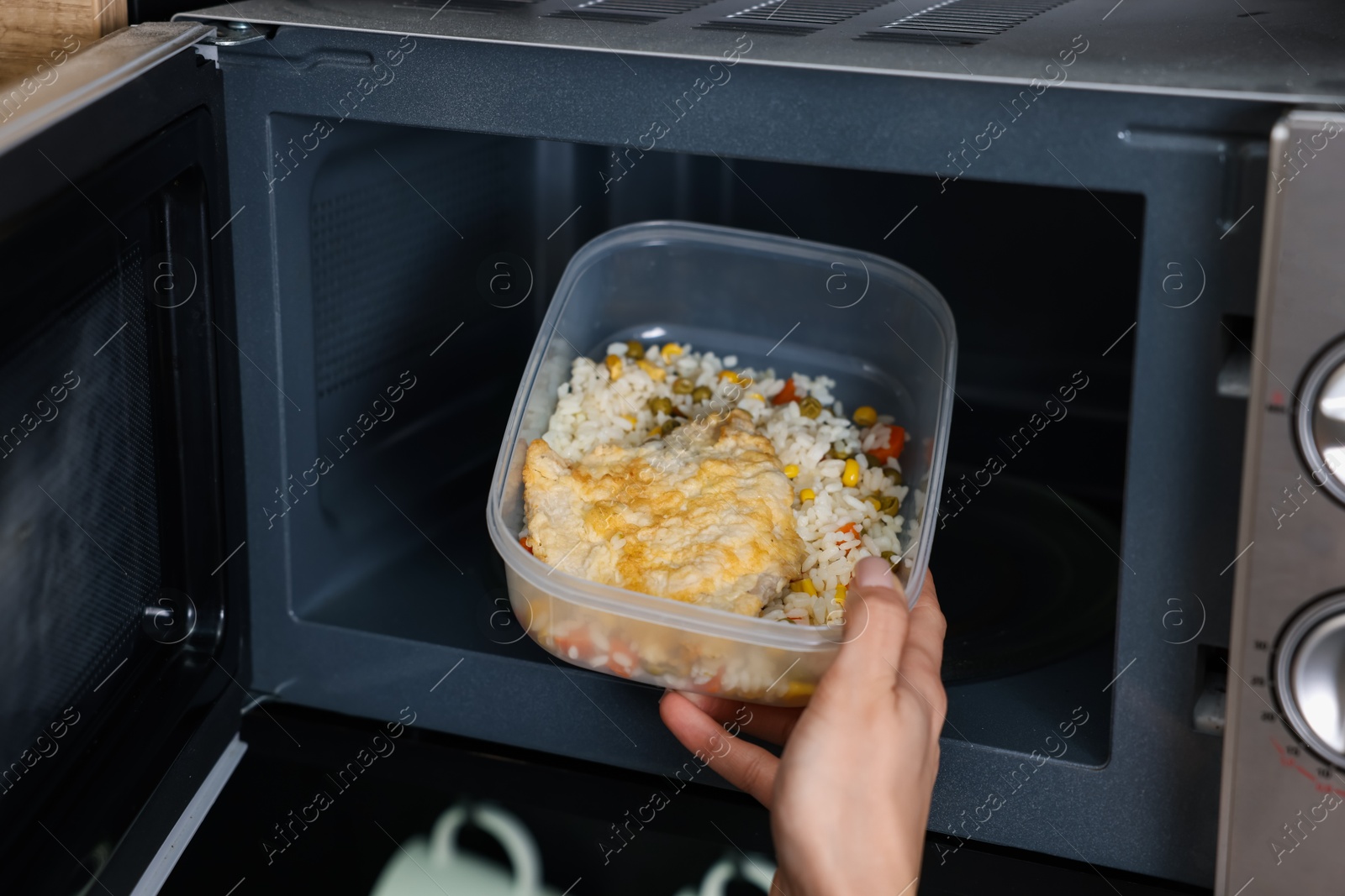 Photo of Woman putting container with lunch into microwave indoors, closeup